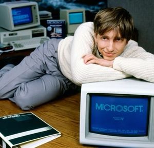 A young Bill Gates casually leaning on top of a CRT monitor, with a prominent Microsoft logo on screen.