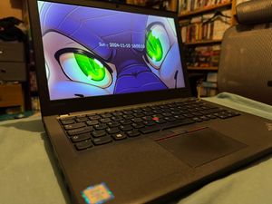 A ThinkPad X270 on a bed, displaying a custom lock screen with a dragon staring intensely.