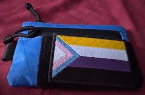 An Alpaka zip pouch with a velcro patch with a trans and non-binary variant of the Progress pride flag